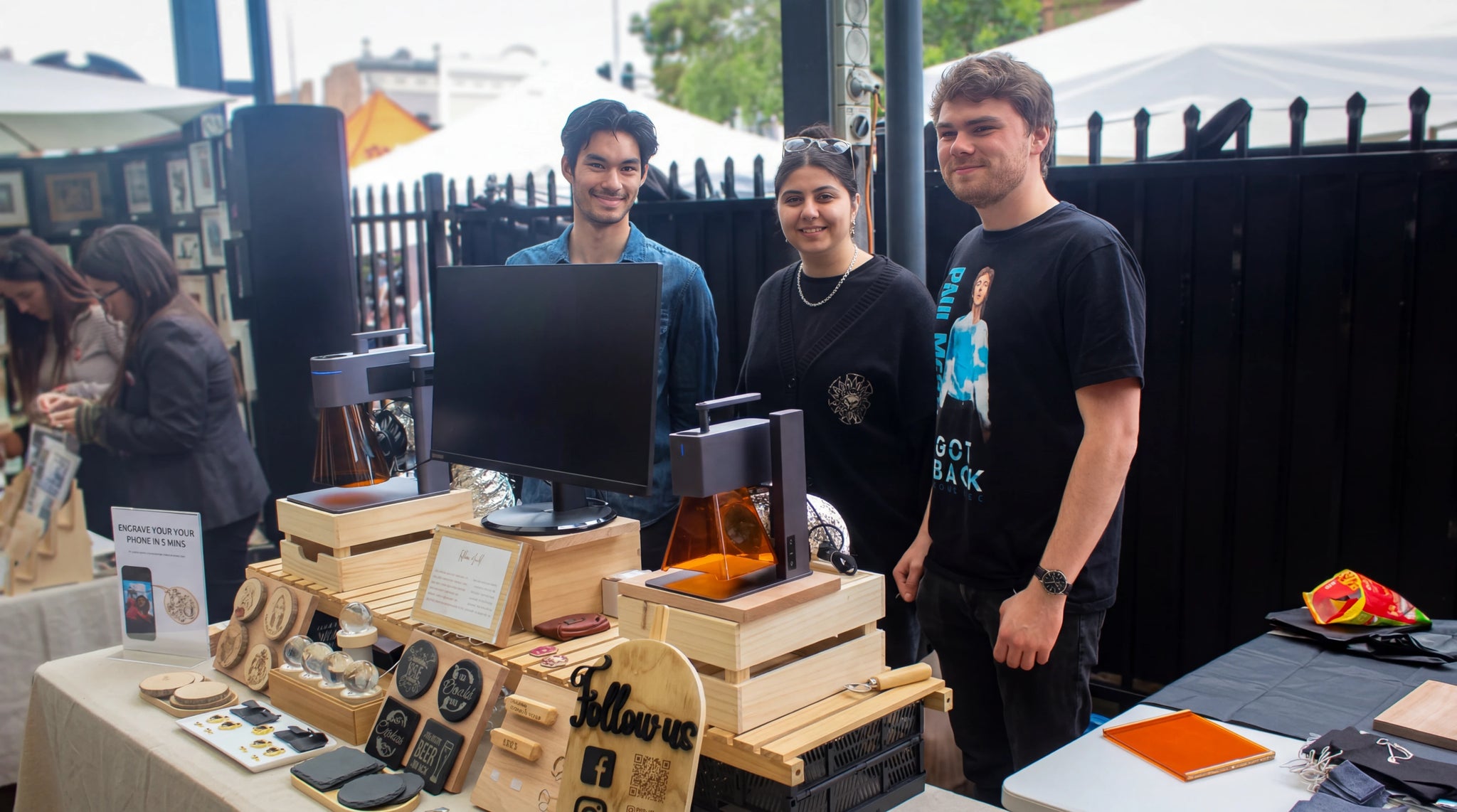 Three sellers beside their stand, demonstrating machines and craft products.