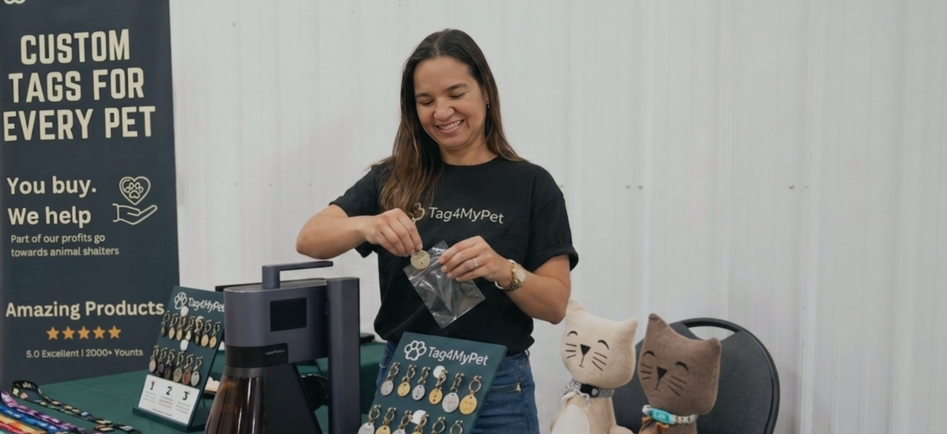 A woman presenting custom pet tags with a LaserPecker machine at a craft market booth.